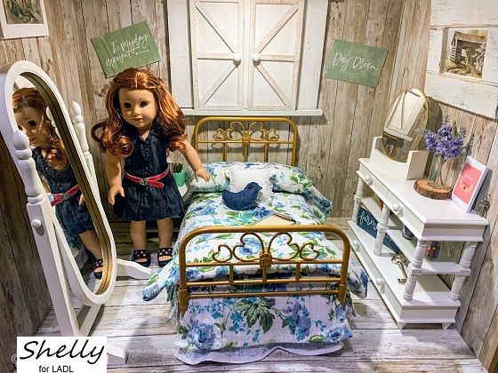 a doll standing in front of a bed with a mirror on the wall next to it