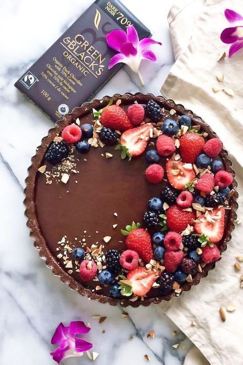 a chocolate tart topped with fresh berries and nuts next to a bar of chocolate