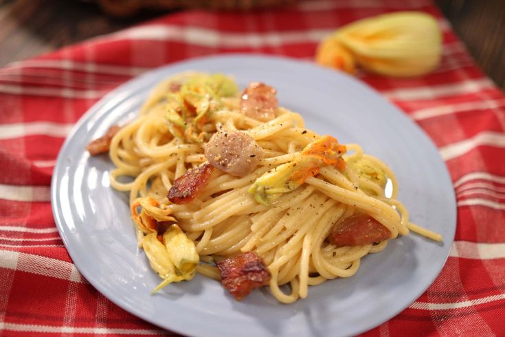 a plate of pasta with bacon and broccoli on a red checkered table cloth