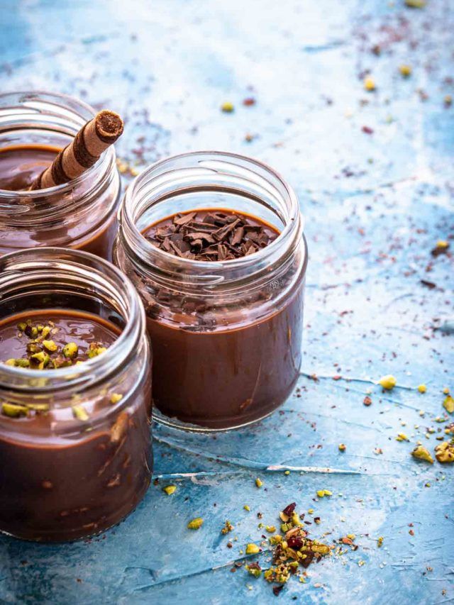 three jars filled with chocolate pudding on top of a blue countertop next to cinnamon sticks