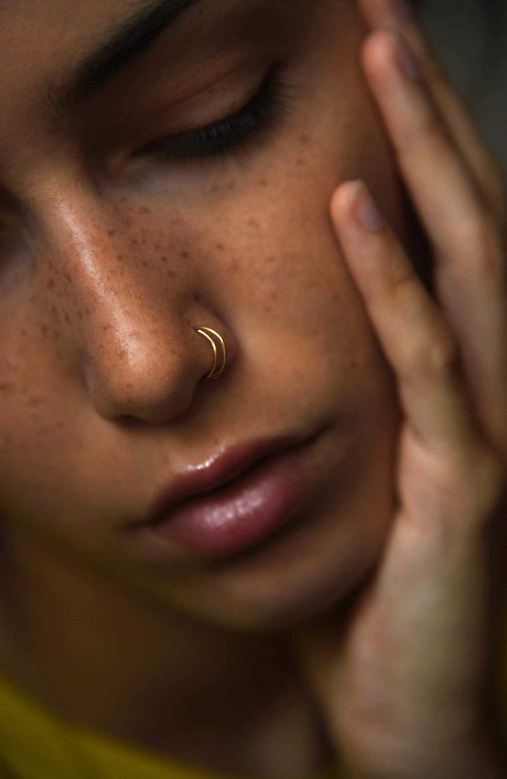 a close up of a person with a nose ring on their left side and her right hand near her face