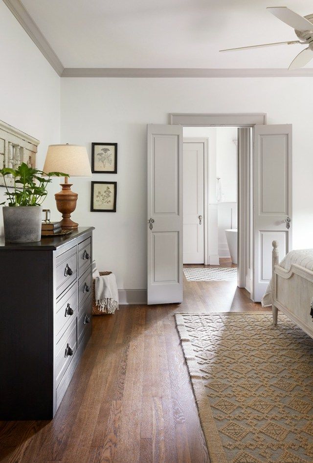 a bedroom with white walls and wood flooring has a ceiling fan in the corner