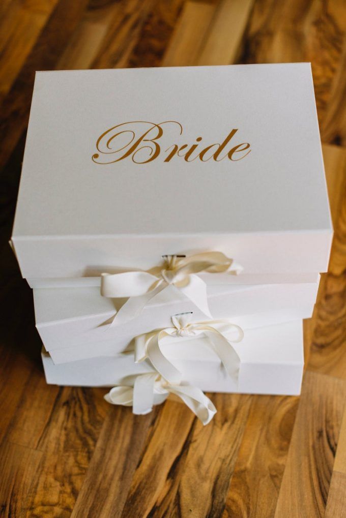 a white box with gold lettering on the lid and ribbon tied around it, sitting on a wooden floor