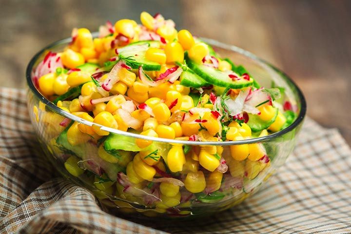 a glass bowl filled with corn and cucumbers