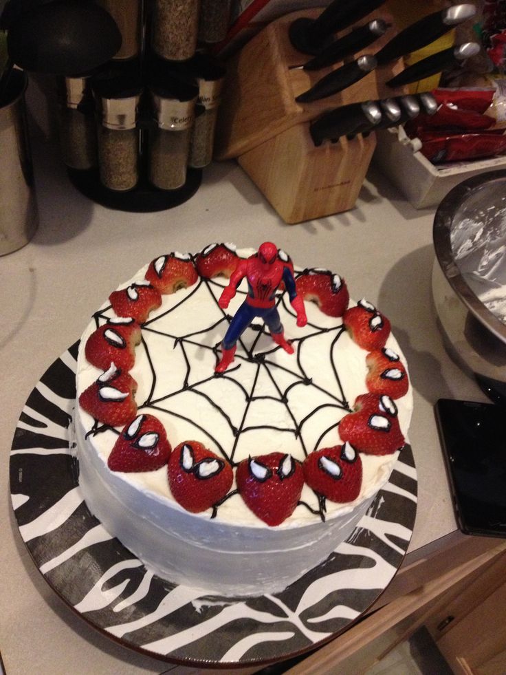 a spiderman cake with strawberries and cream frosting on a black and white plate