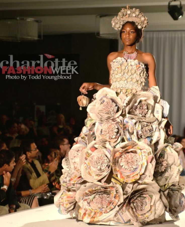 a woman in a dress made out of newspaper rolls on the runway at charlotte fashion week