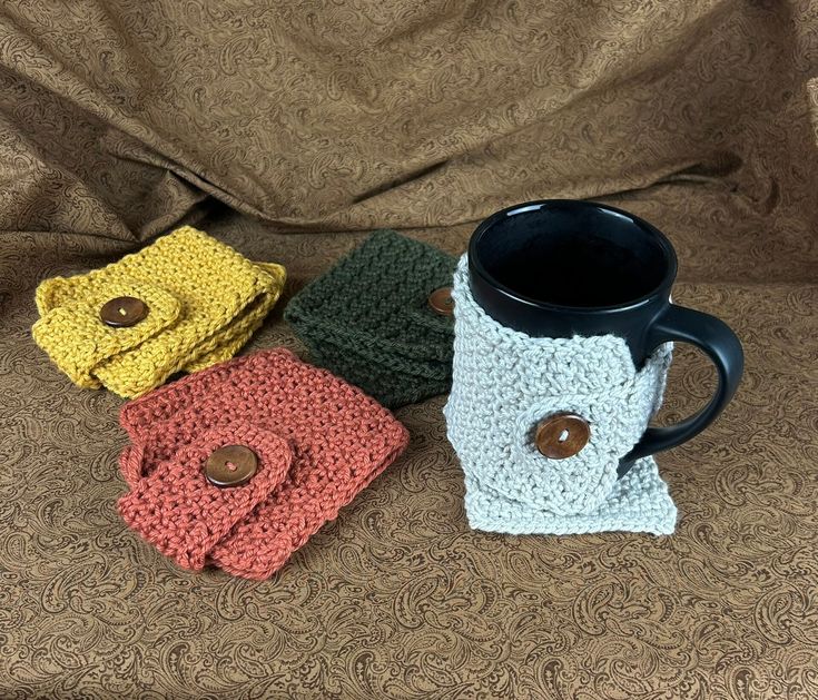 three crocheted coffee mug cozyies sitting on a couch next to each other