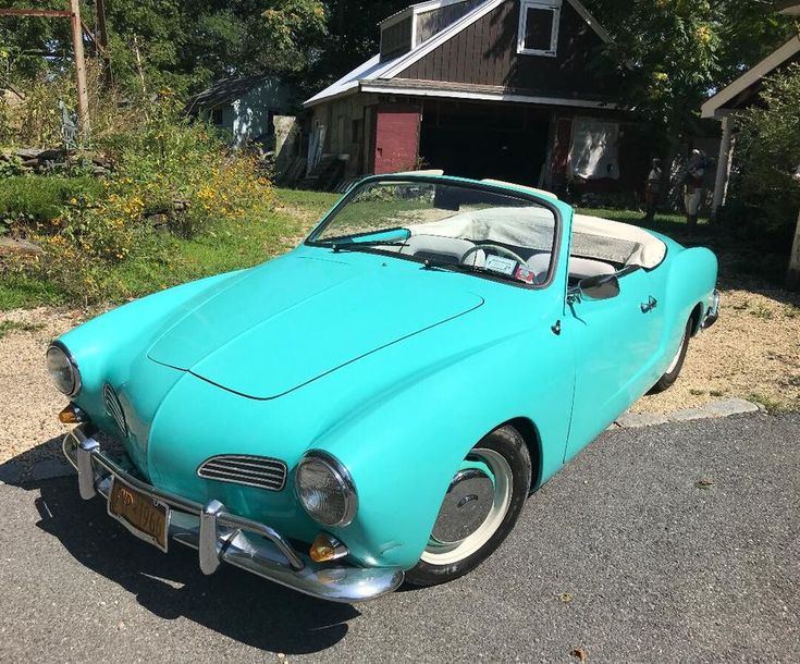 an old blue sports car parked in front of a house on the side of the road