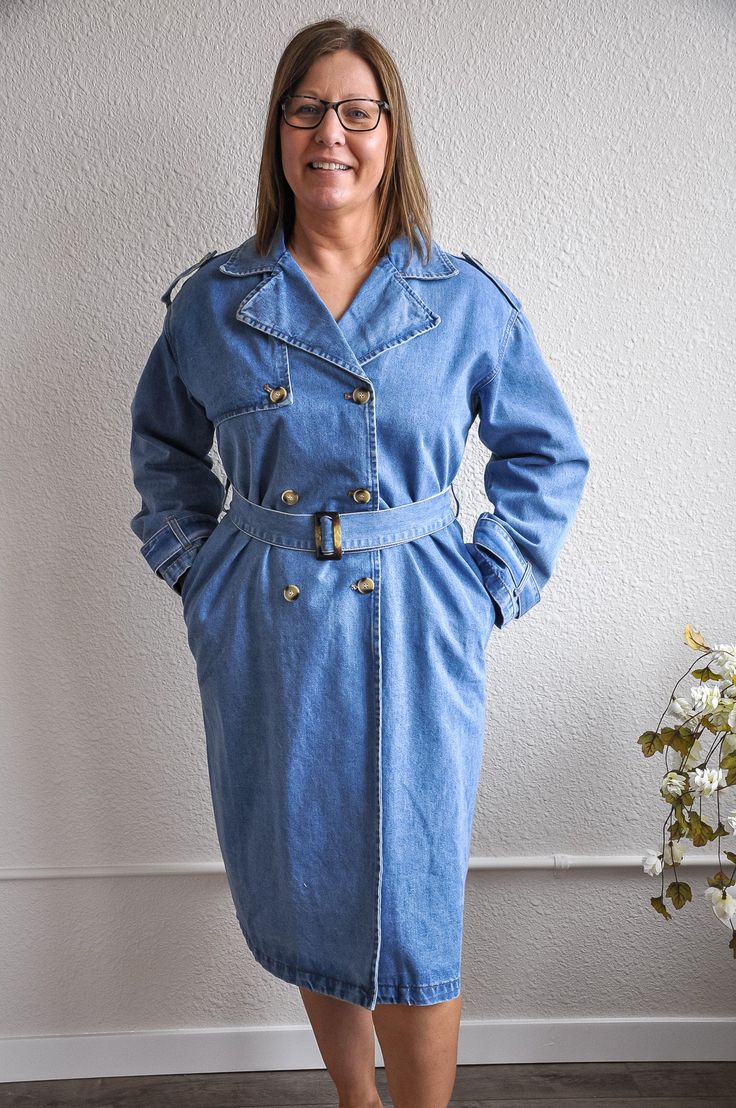 This medium denim trench coat exudes timeless elegance and casual sophistication. The medium denim wash gives it a classic yet contemporary look, while the waist belt detail adds a touch of tailored refinement, allowing for a customizable fit. With its long denim coat fit, this piece offers both warmth and style, making it a versatile addition to any wardrobe. The classic button closure and long sleeves provide a traditional trench coat silhouette, perfect for layering over various outfits. The Denim Outerwear With Belt Loops For Work, Belted Denim Blue Outerwear For Fall, Belted Blue Denim Outerwear, Blue Belted Denim Outerwear, Long Sleeve Denim Outerwear With Belt Loops, Belted Denim Jacket For Workwear, Denim Jacket With Belted Cuffs, Long Sleeve Denim Jacket With Belted Cuffs, Belted Denim Blue Denim Outerwear