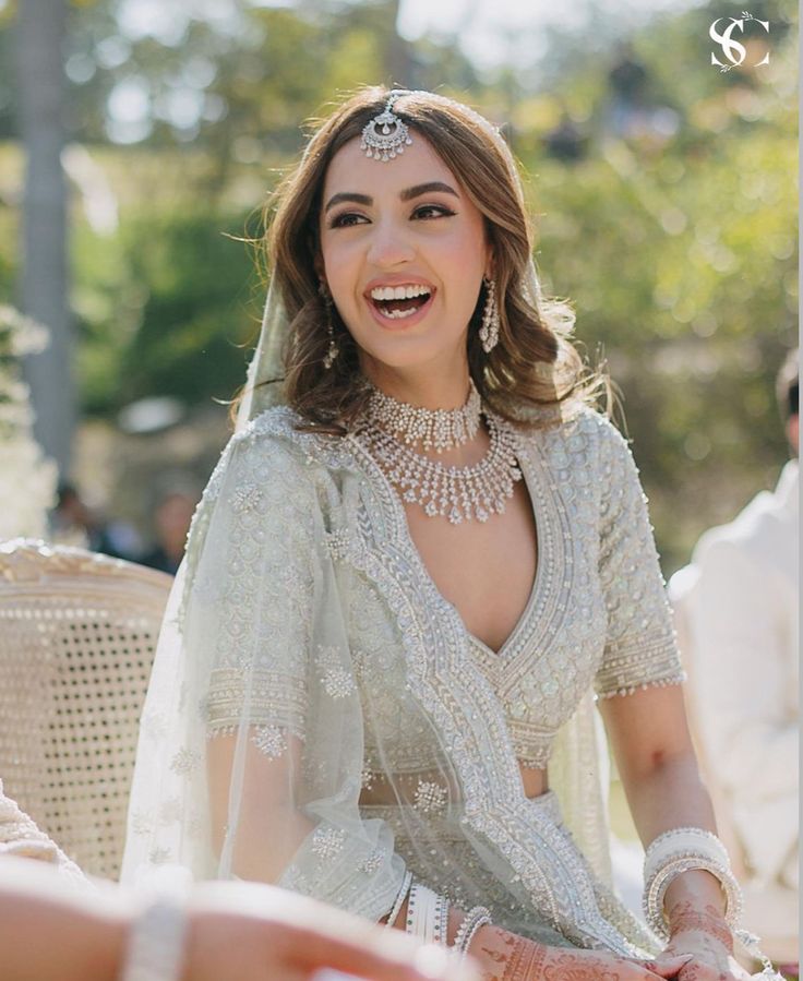 a woman in a bridal gown smiles as she sits on a chair with her hands together