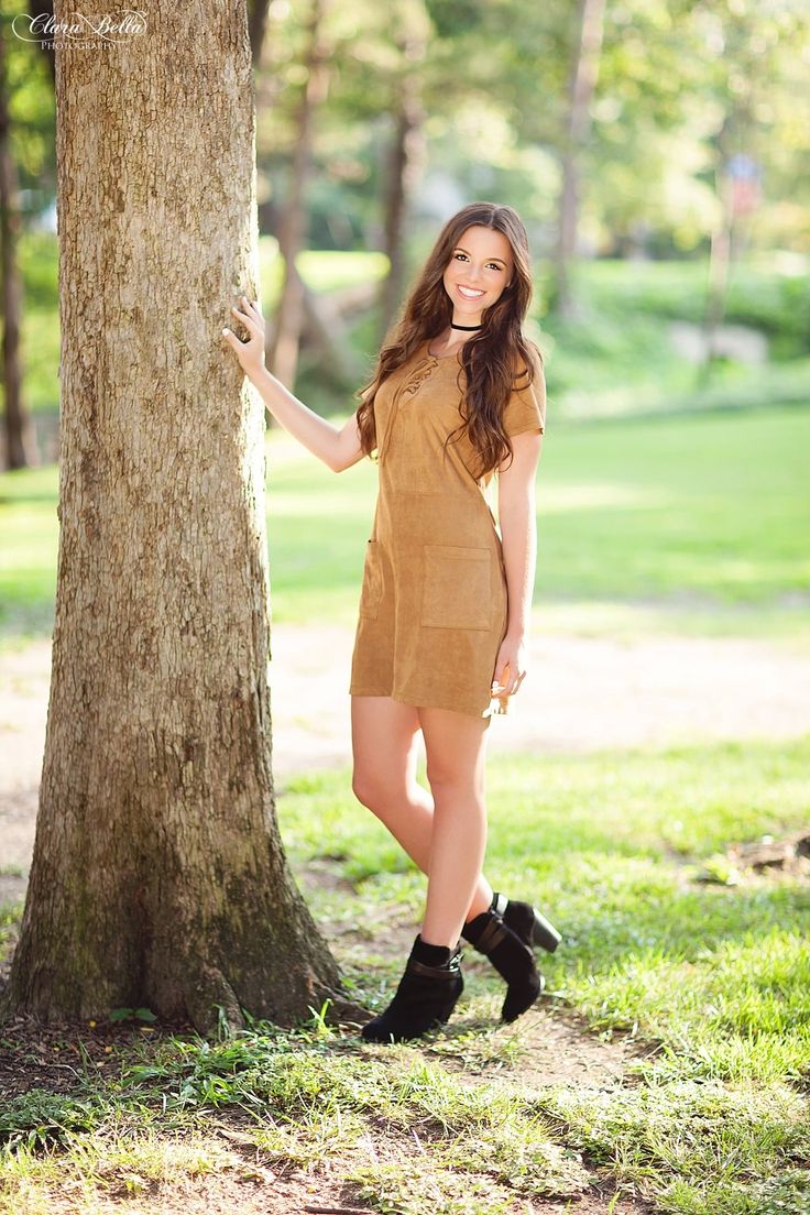 a beautiful young woman standing next to a tree