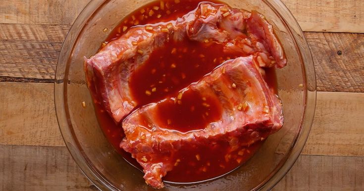 two pieces of raw meat in a glass bowl on a wooden table with ketchup