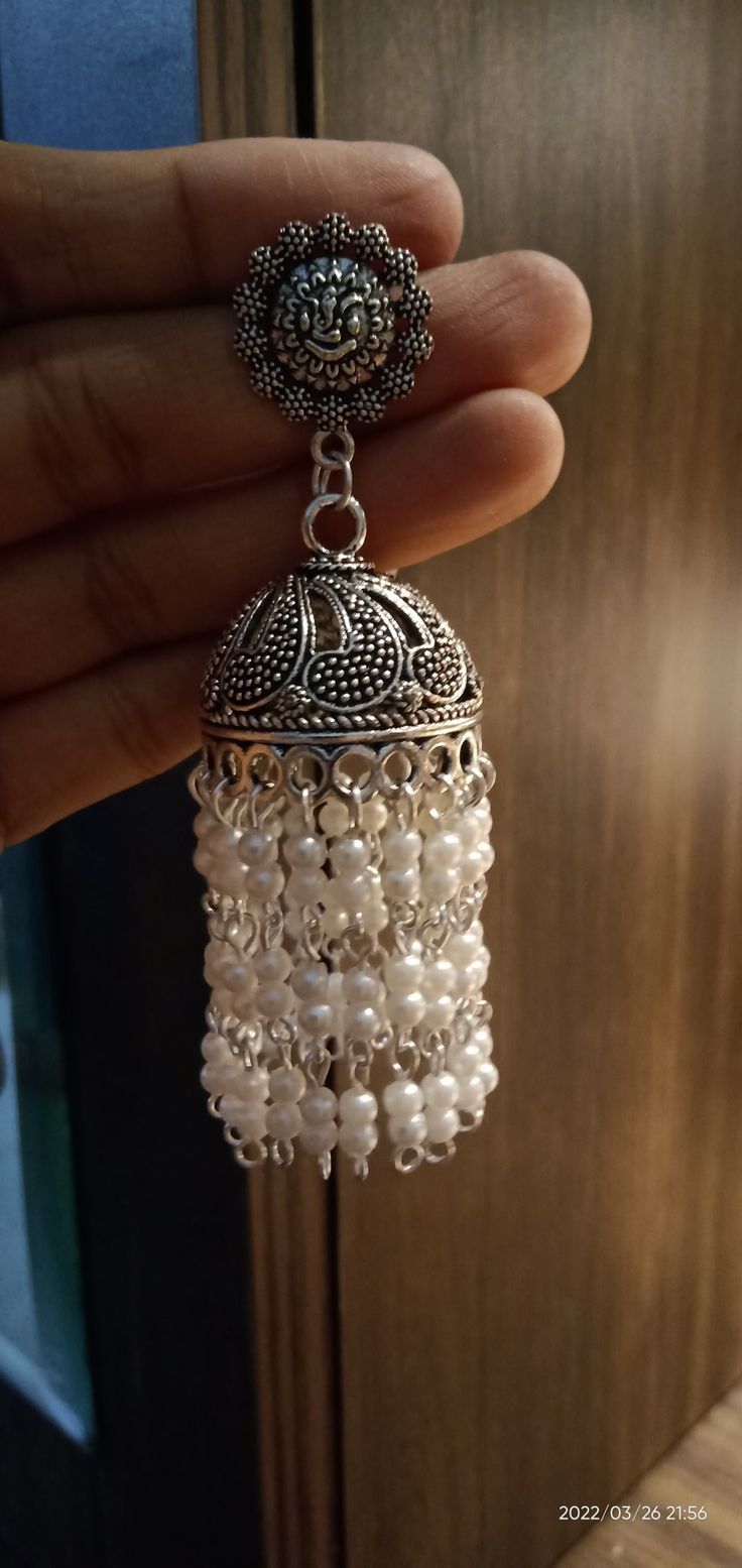 a hand holding a small white beaded bell with pearls hanging from it's side