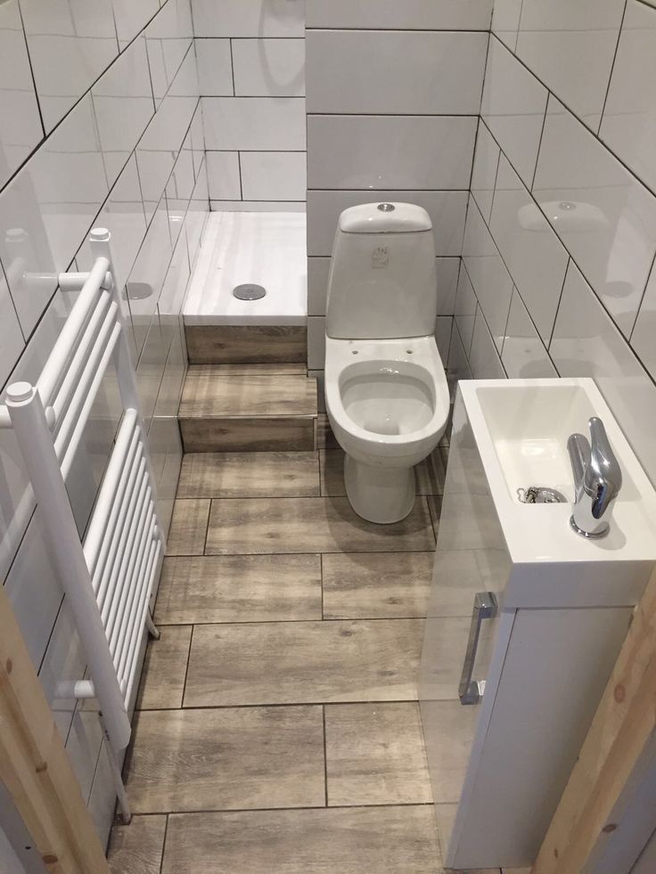 a toilet and sink in a bathroom with white tiles on the walls, wood flooring