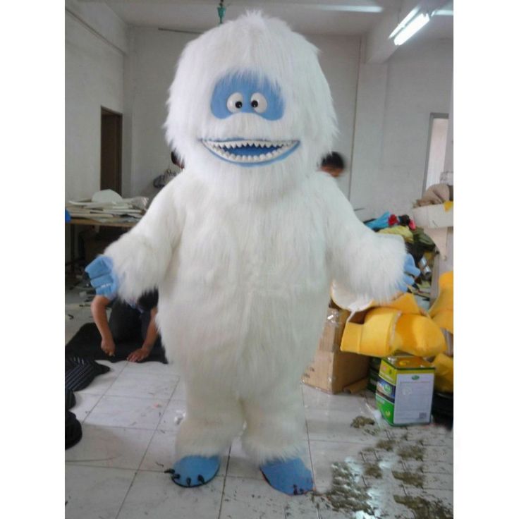 a man standing next to a big furry white monster in a room with other people