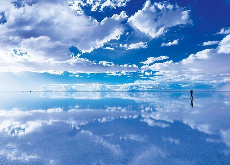 a person standing in the middle of a large body of water under a cloudy blue sky