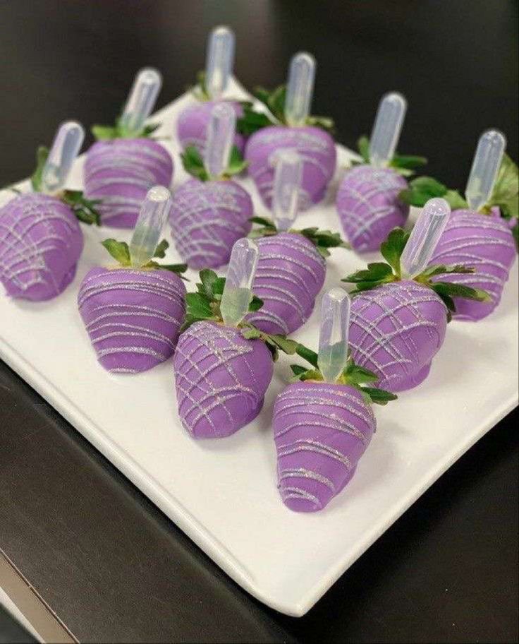 purple strawberries are arranged on a white platter with green leaves in the middle