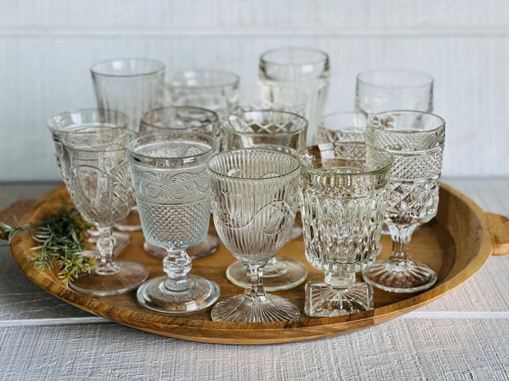 a wooden tray topped with lots of glassware on top of a white tablecloth