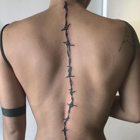 the back of a man with barbed wire on his neck and shoulder, behind him is a cross tattoo