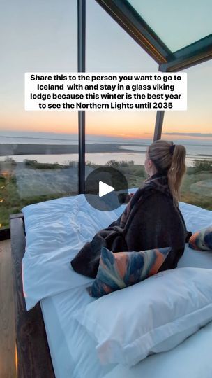 a woman sitting on top of a bed in front of a large window overlooking the ocean