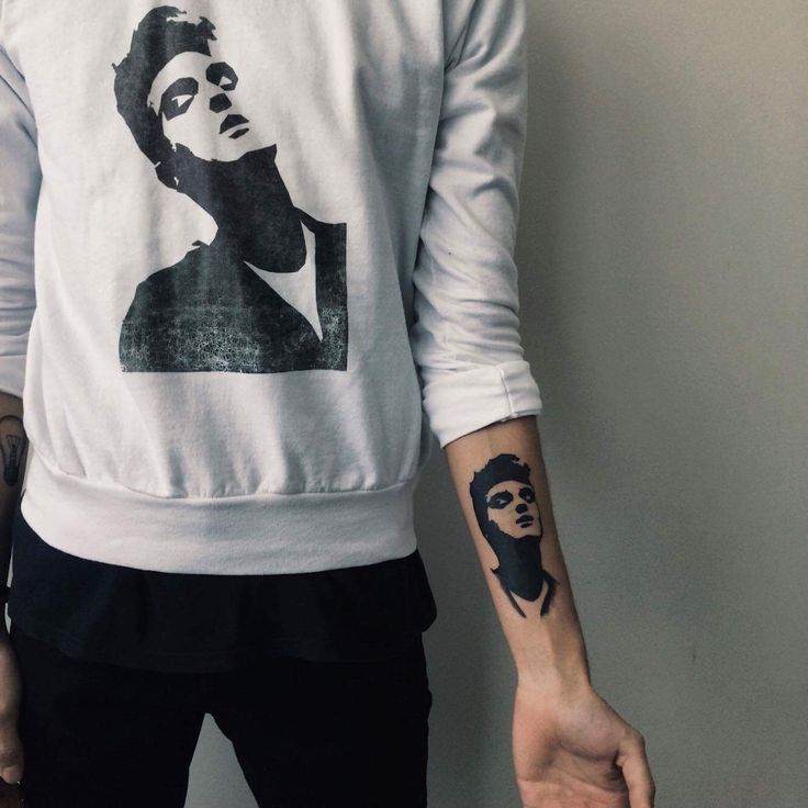 a man with a tattoo on his left arm wearing a white sweatshirt and black pants