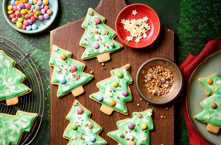 christmas cookies decorated with green icing and sprinkles on a wooden cutting board