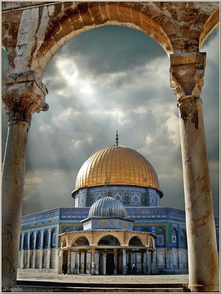 the dome of the rock is seen through an arch in front of a cloudy sky