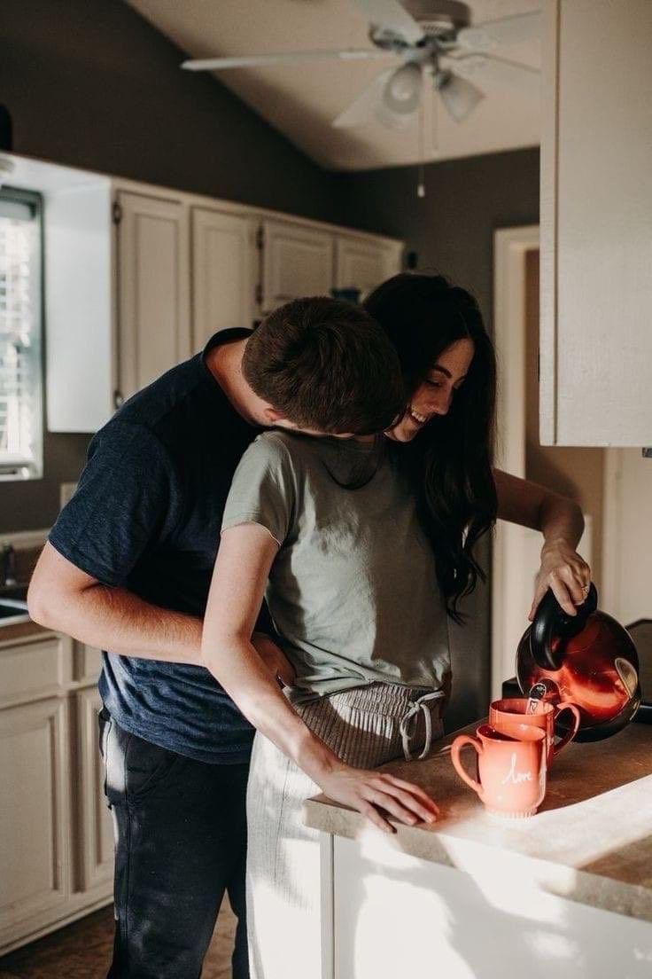 a man and woman standing in a kitchen next to an orange teapot on a counter