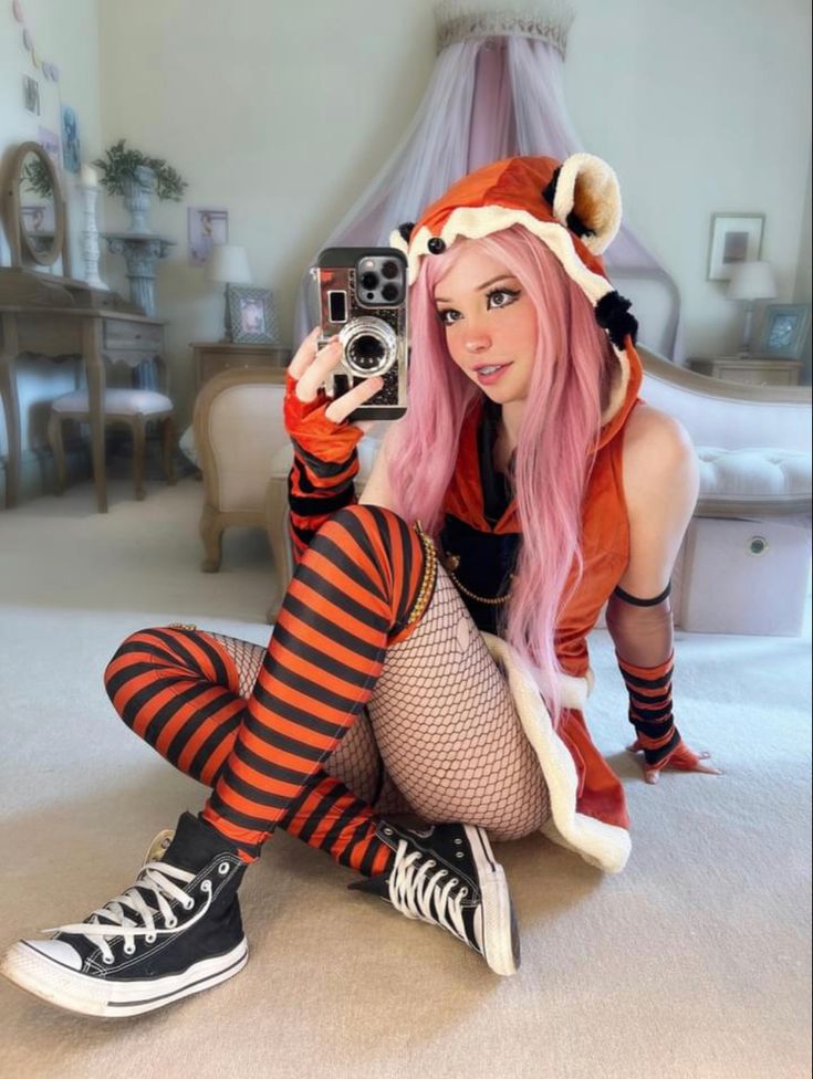 a woman with pink hair is taking a selfie in her bedroom while wearing an orange and black striped outfit