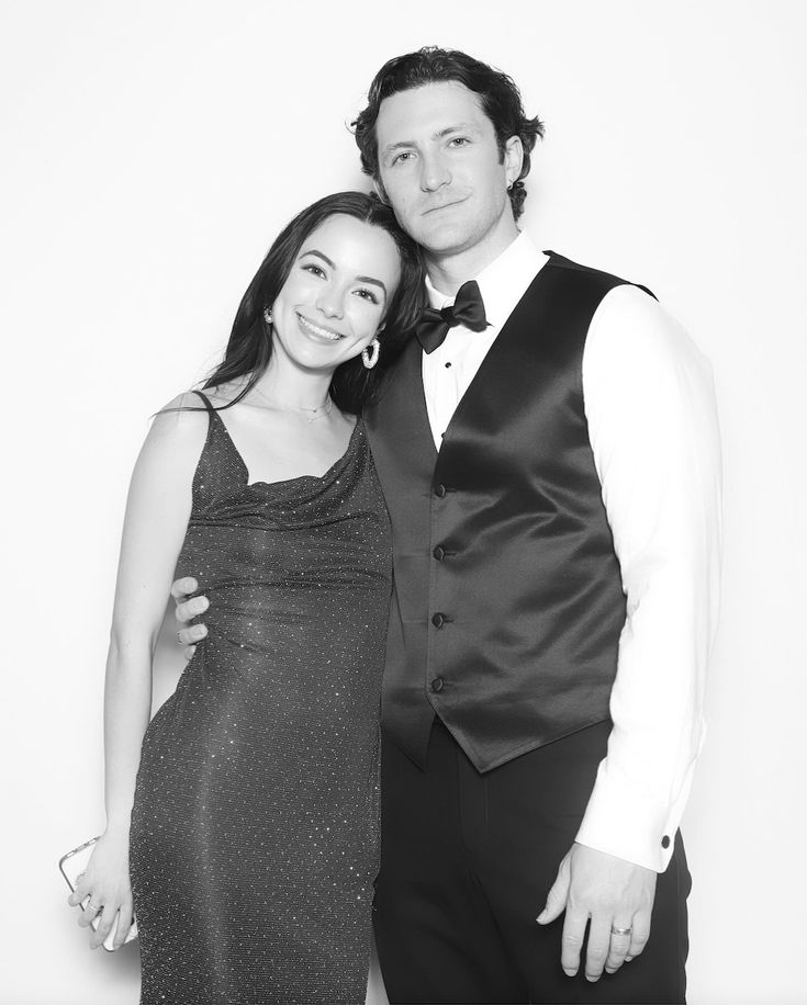 a man and woman are posing for a photo in black and white attire, one is wearing a tuxedo while the other wears a dress