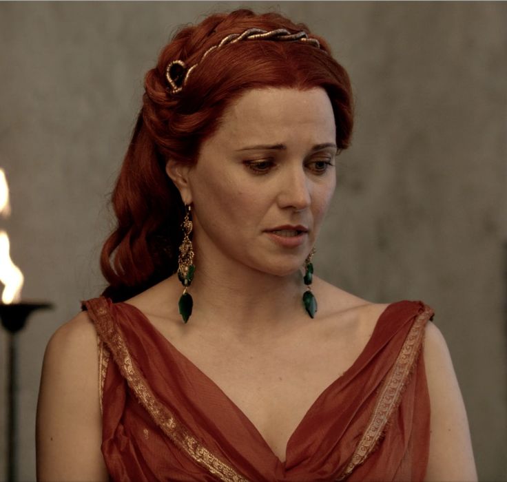 a woman with red hair wearing a tiara and green earrings in front of a lit candle