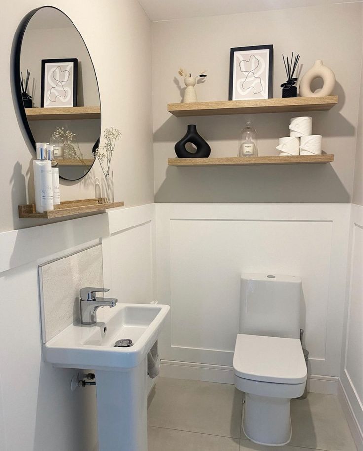 a white toilet sitting next to a sink in a bathroom under a mirror and shelves