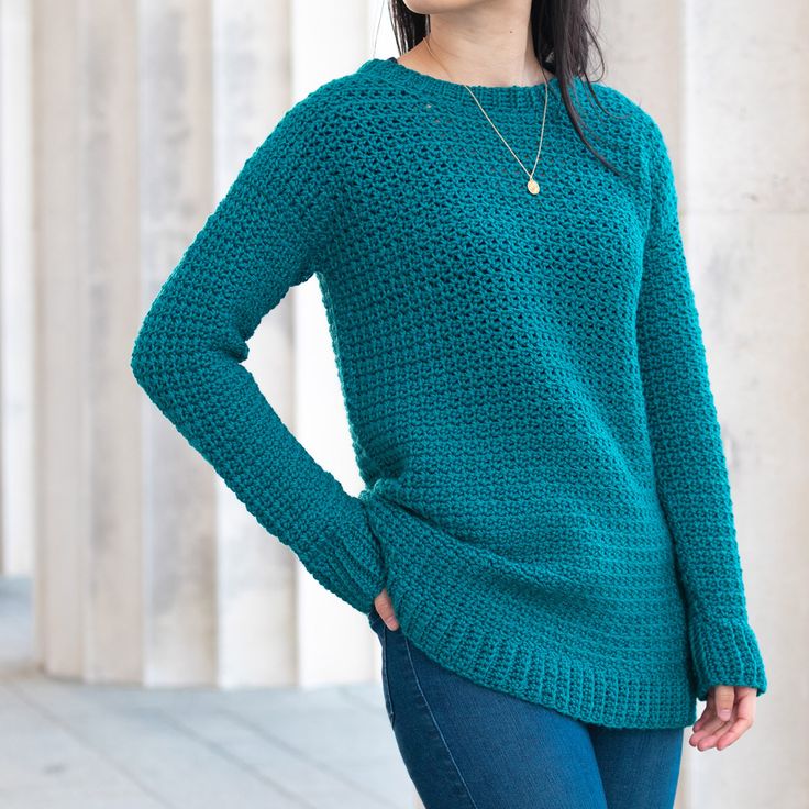 a woman standing in front of columns wearing a green sweater and jeans with her hands on her hips