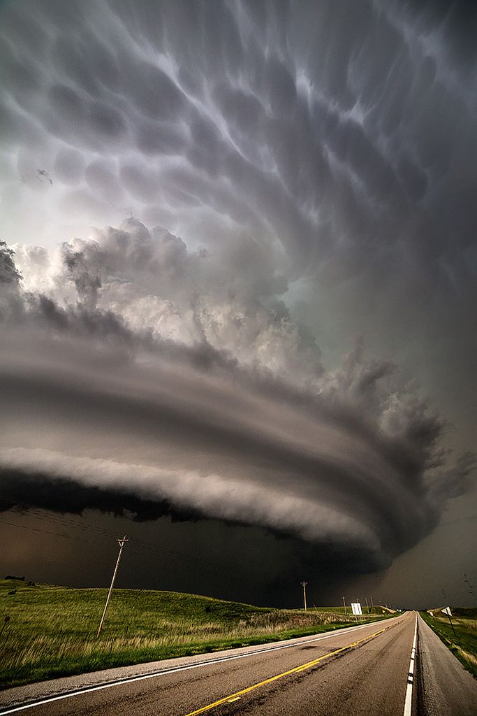 an image of a storm coming in from the sky over a road and grassy field