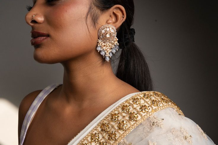 Dress up your outfits with our opulent Grey Nirvi Earrings. Handcrafted with high-quality Pachi Kundan, pearls and crystals on Gold plating, these earrings are a must-have in your jewelry box. Specifications Materials used: Pachi Kundan, pearls, crystals, Gold plating At Romikas, we pride ourselves on the craftsmanship and high quality of our jewelry, designed to enhance your natural beauty. Please contact us with any questions. Elegant Danglers For Festive Reception, Elegant Danglers For Reception And Festive Occasions, Elegant Danglers With Stone Work For Reception, Elegant Chandbalis With Stone Work, Elegant Bridal Chandbali Meenakari Earrings, Elegant Pearl Drop Danglers For Reception, Elegant Pearl Meenakari Earrings For Diwali, Elegant Chandbali Danglers For Reception, Elegant Meenakari Bridal Earrings For Diwali