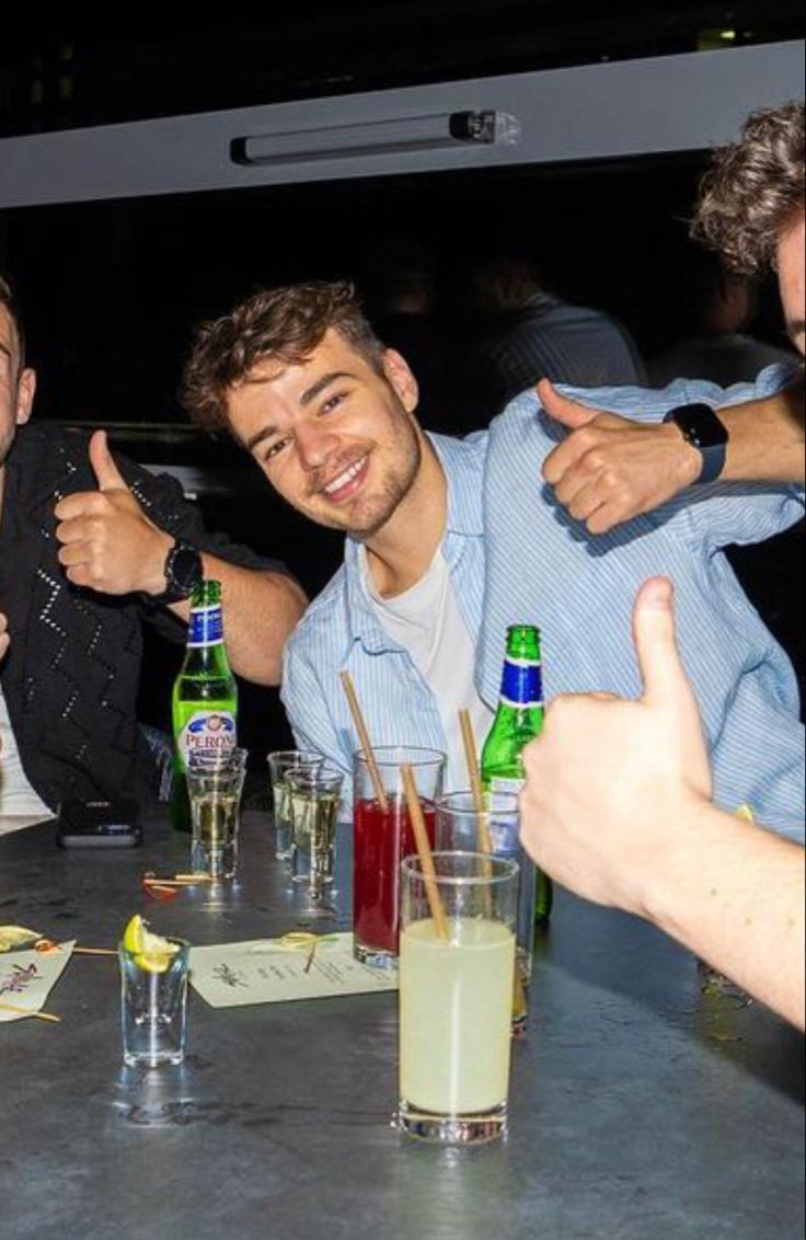 three men sitting at a table with drinks in front of them giving the thumbs up sign