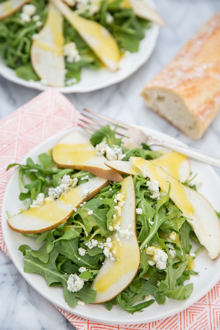 two white plates topped with green salad and sliced apples