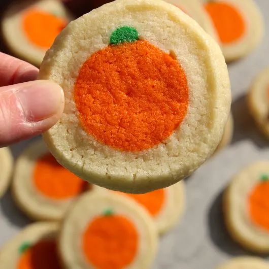 a person holding up a small cookie with an orange painted on it