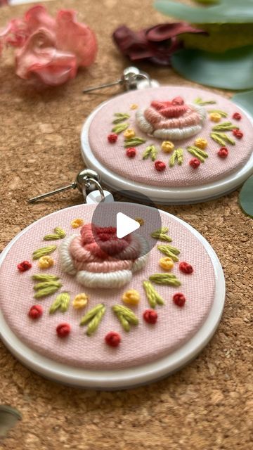 two pink hoop earrings with flowers and leaves on the bottom one has a button in the middle