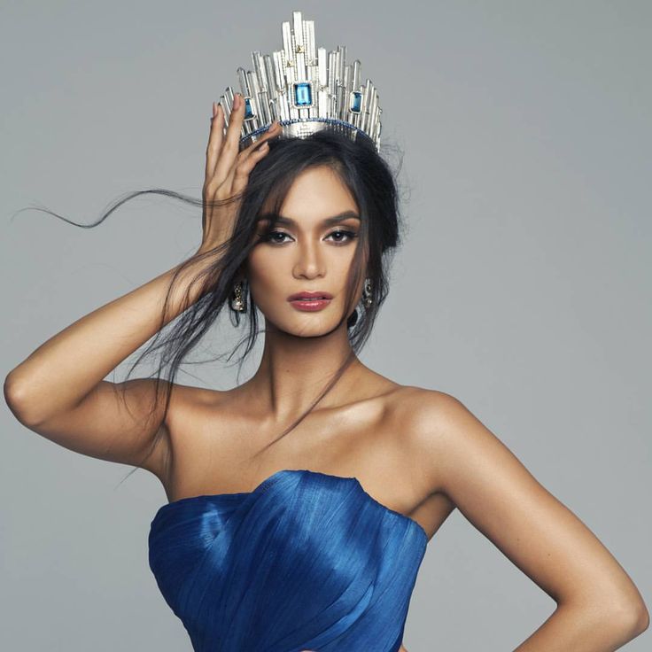 a woman in a blue dress with a tiara on her head and hands behind her head