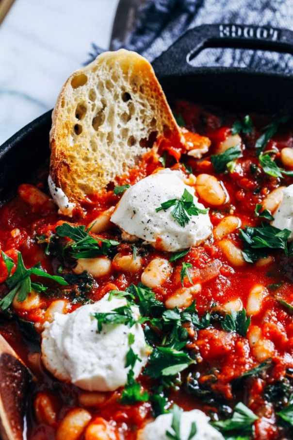 a skillet filled with beans and cheese on top of a wooden spoon next to bread