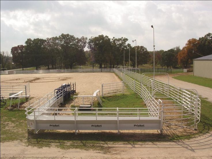 an animal pen in the middle of a dirt field with grass and fence around it