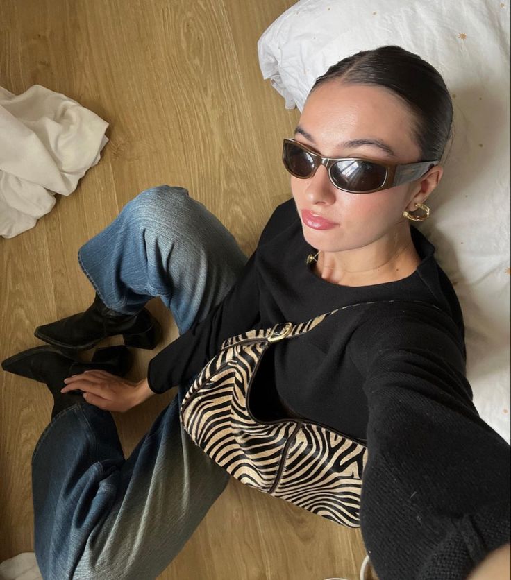 a woman laying on the floor with her legs crossed wearing sunglasses and black sweater, jeans and high heeled shoes