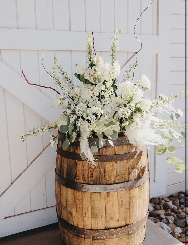 a wooden barrel with white flowers and greenery in it next to a barn door