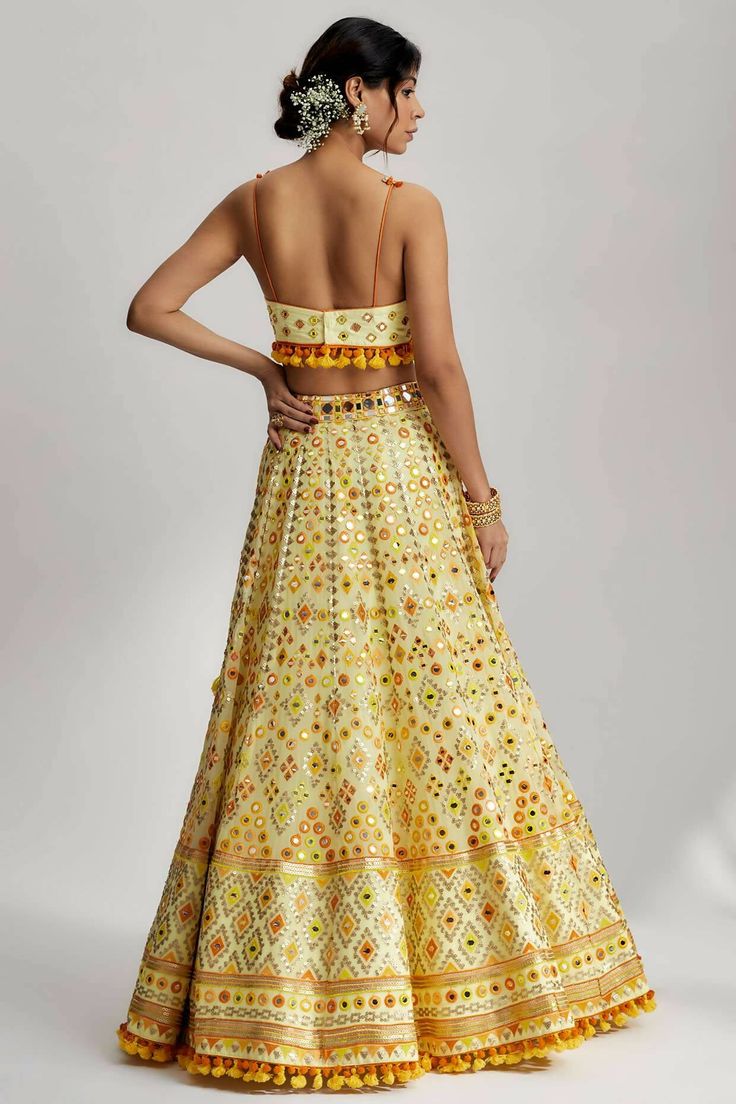 To further enhance its beauty, the ashi lehenga is adorned with pompoms and tassels. These playful elements add a whimsical touch and create a sense of movement as you glide across the dance floor. The pompoms and tassels are meticulously crafted and delicately attached, ensuring they stay in place throughout your glamorous wedding ceremony. Yellow Bohemian Lehenga For Festive Occasions, Bohemian Party Lehenga With Mirror Work, Bohemian Embellished Lehenga For Party, Bohemian Embellished Lehenga For Weddings, Bohemian Embellished Wedding Lehenga, Yellow Embellished Traditional Wear For Festive Occasions, Traditional Dress With Tassels For Diwali, Bollywood Anarkali Set With Tassels For Festivals, Bohemian Yellow Lehenga For Festive Occasions