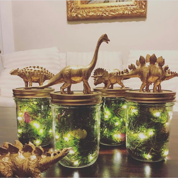 four glass jars with dinosaurs in them on a table next to a gold dinosaur figurine