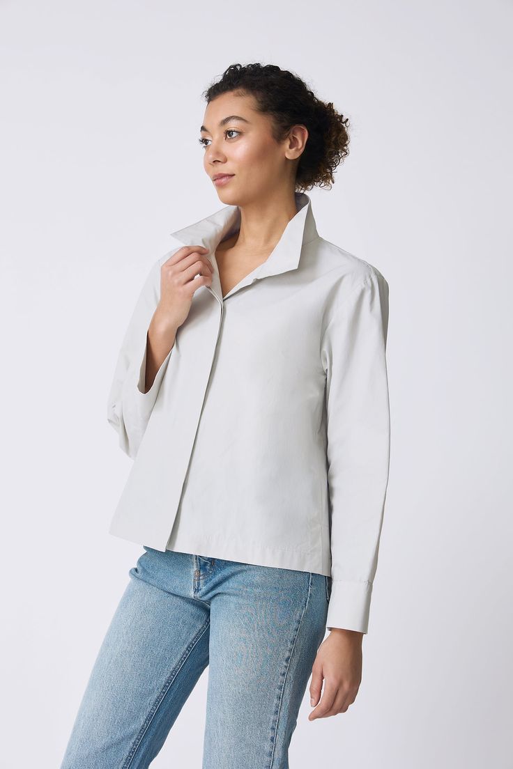 Meet the perfect transition style into the warmer days. Our Peggy Collared Shirt can be worn as a top or as a light outer layer. Made in our Italian Broadcloth, this style has a high collar with plenty of attitude, a drop shoulder fit, back pleat, and side slits for ease of wear. Drop shoulder fit, high stand collar, hidden button front placket, back yoke with inverted pleat, side slits on body - 51% Cotton, 49% Nylon - Fabric woven in Italy - Made in NYC - Dry clean or machine wash - Our model Spring Cotton Blouse With Fold Down Collar, Spring Daywear Blouse With Fold Down Collar, Layering Cotton Tops With Placket, Chic Cotton Shirt For Layering, Spring Layering Shirt With Collar, Modern Fall Shirt For Daywear, Lapel Collar Shirt For Daywear In Fall, Spring Blouse For Layering With Shirttail Hem, Spring Collared Blouse With Placket