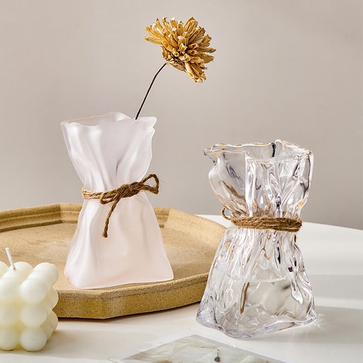 a glass vase with a flower in it next to some candles on a tray that is sitting on a table