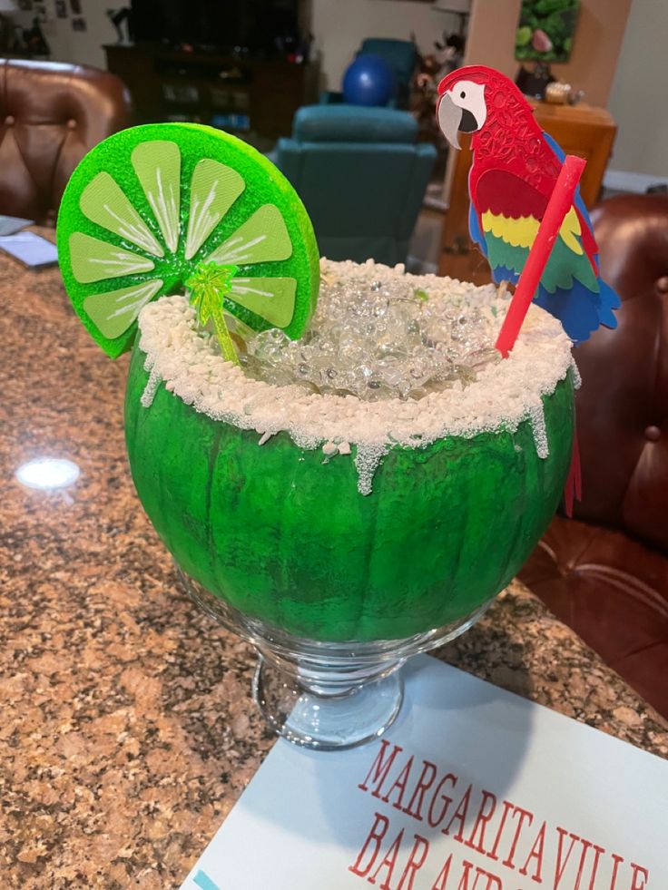 a margarita drink with lime and a red parrot on the top is sitting on a table