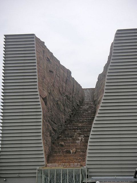 two tall buildings with steps leading up to them in front of a large rock face